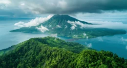 Majestätischer Blick auf den Krater des Ruang Vulkans, umgeben von üppigen tropischen Wäldern, nebelhaften Wolken und dem tiefblauen Meer der Insel Nord-Sulawesi.